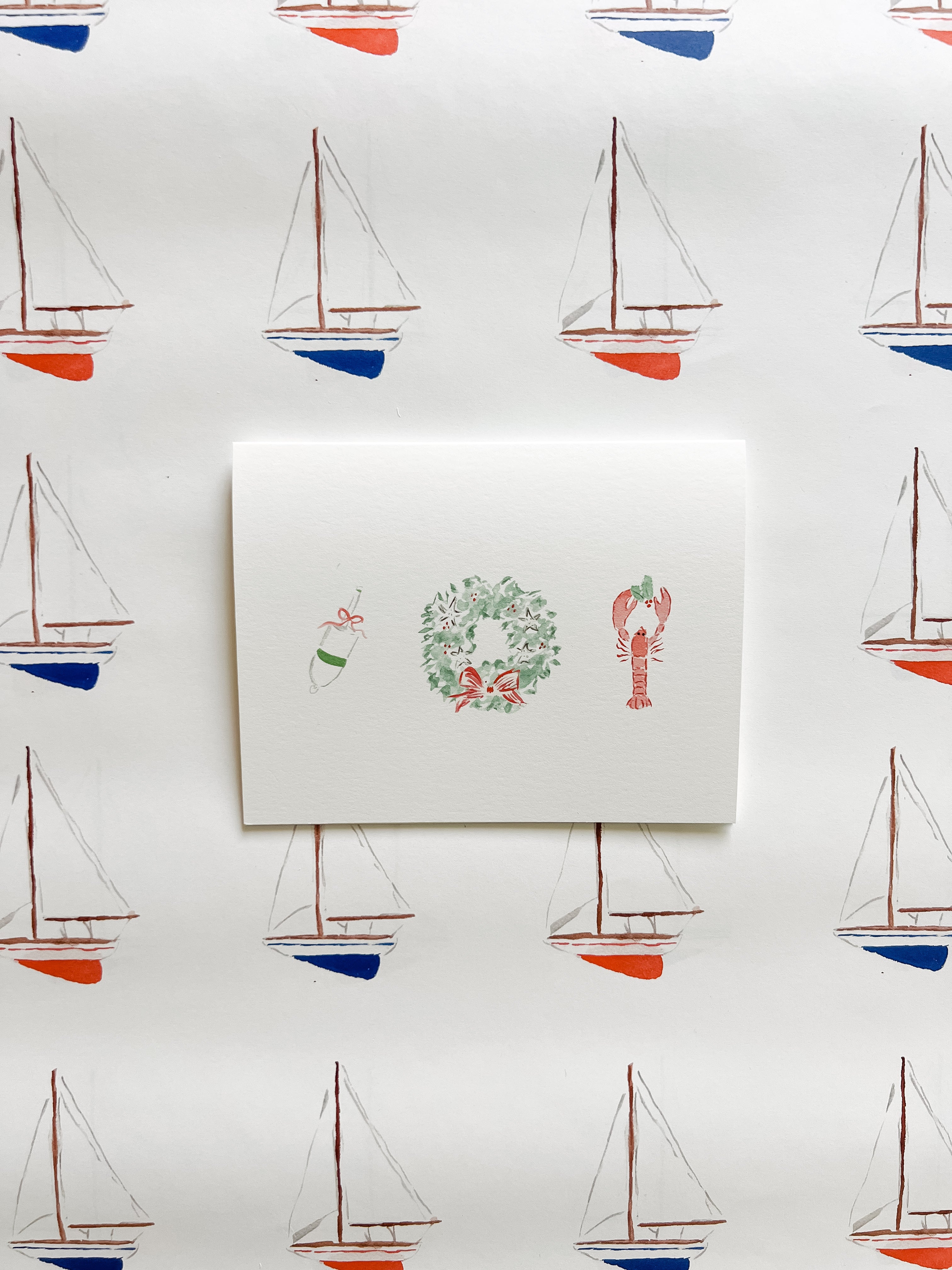 White card with illustrations of a wreath, lobster, and buoy on a background of sailboat patterns.