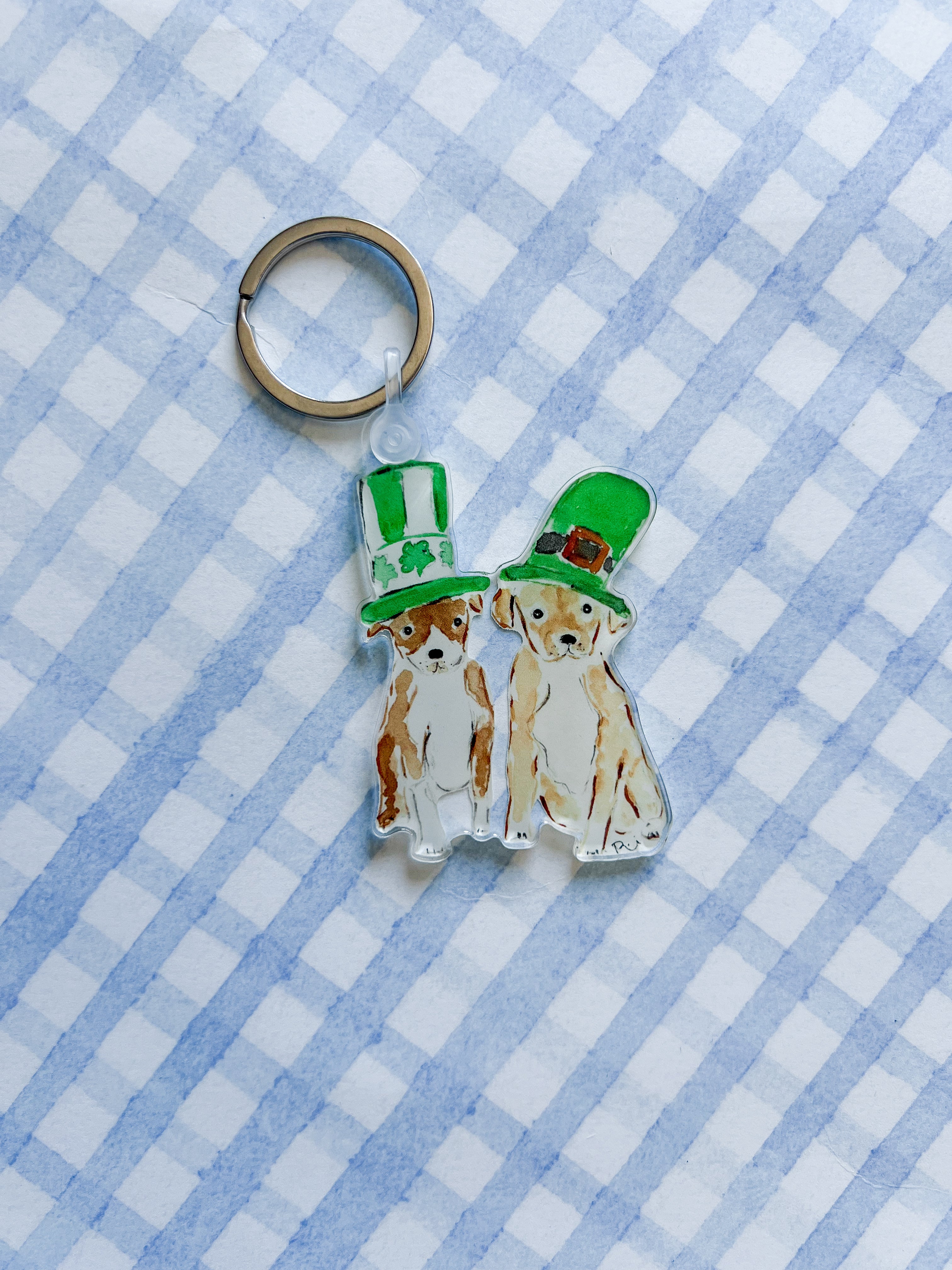 Two dog-shaped keychains with green hats on a blue and white checkered background